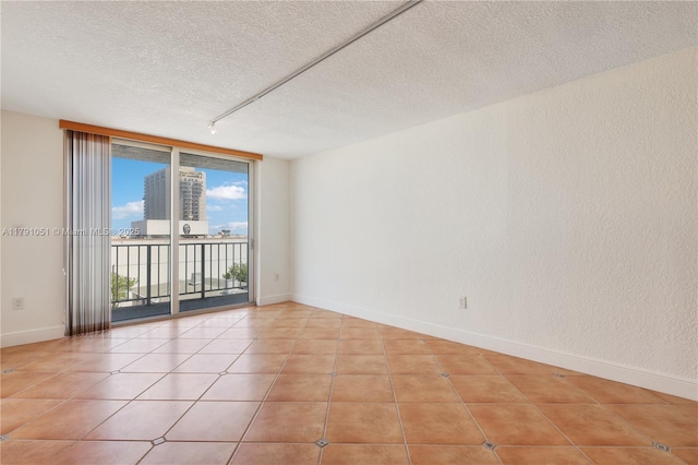 empty room featuring baseboards, a textured ceiling, track lighting, and tile patterned floors