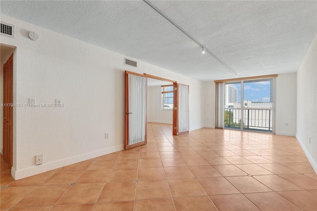 empty room with light tile patterned flooring, a textured ceiling, and visible vents