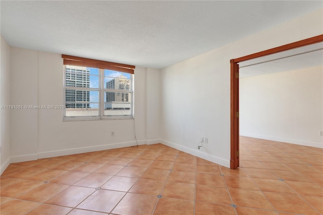 spare room with light tile patterned floors, baseboards, and a textured ceiling