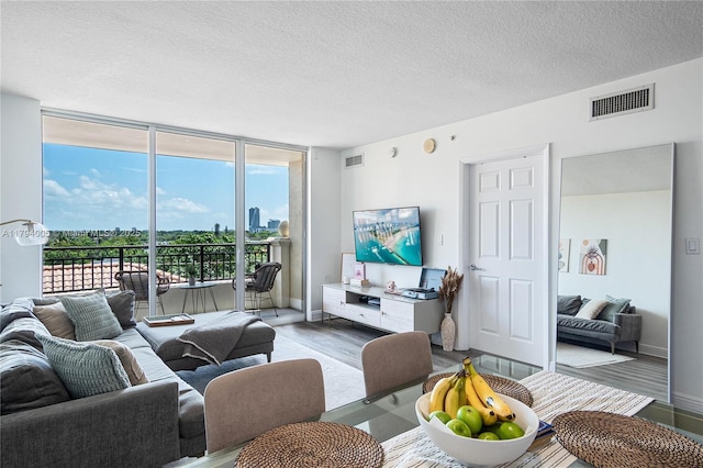 living area with a wall of windows, a textured ceiling, visible vents, wood finished floors, and baseboards