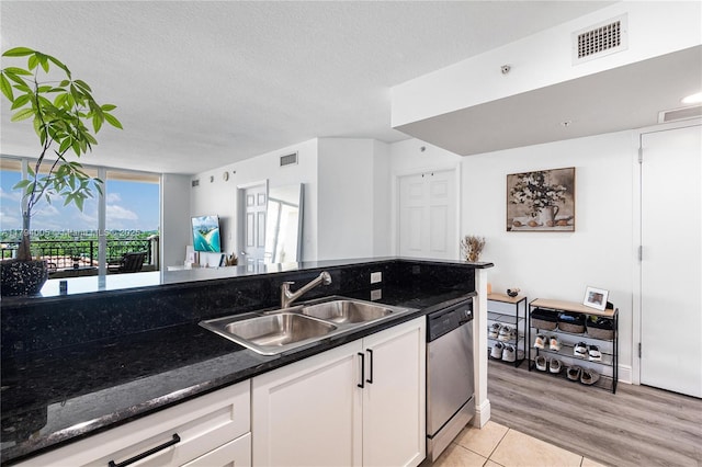 kitchen with stainless steel dishwasher, a sink, white cabinets, and visible vents