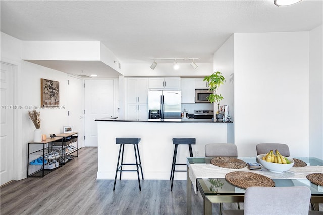 kitchen featuring a peninsula, wood finished floors, dark countertops, white cabinetry, and stainless steel appliances