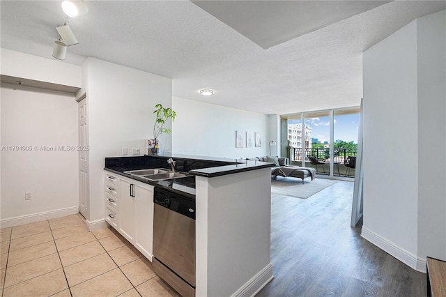 kitchen with dark countertops, stainless steel dishwasher, a sink, baseboards, and open floor plan