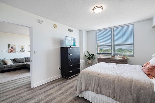 bedroom with baseboards, a textured ceiling, wood finished floors, and visible vents