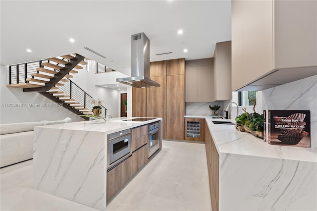 kitchen with oven, light stone counters, a sink, island range hood, and modern cabinets