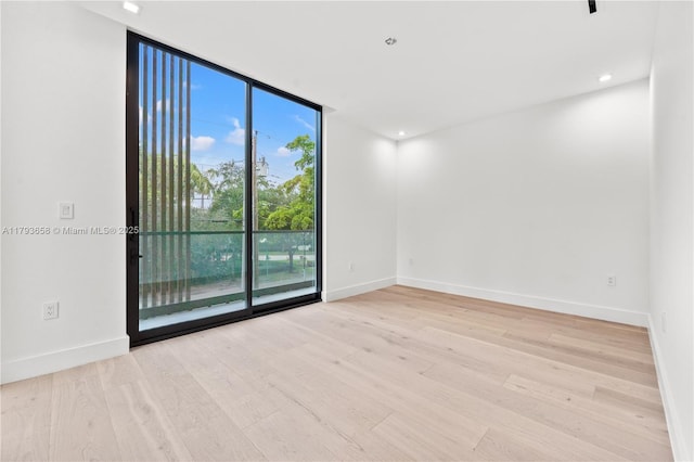 unfurnished room with baseboards, a wall of windows, and wood finished floors