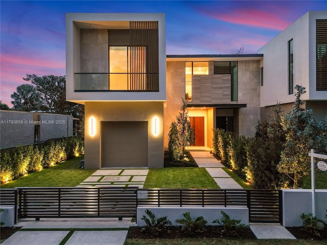 modern home featuring a garage, a fenced front yard, stucco siding, and a front lawn