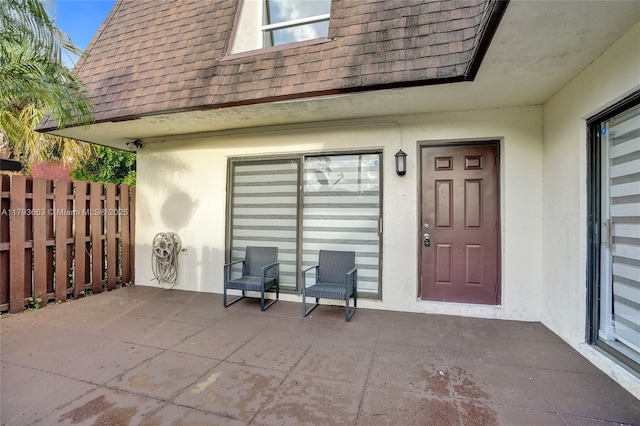 entrance to property featuring a shingled roof, stucco siding, and fence