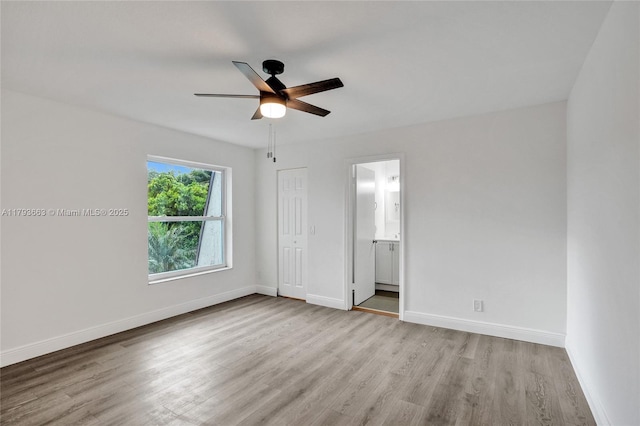 unfurnished bedroom featuring wood finished floors, baseboards, ensuite bathroom, and ceiling fan