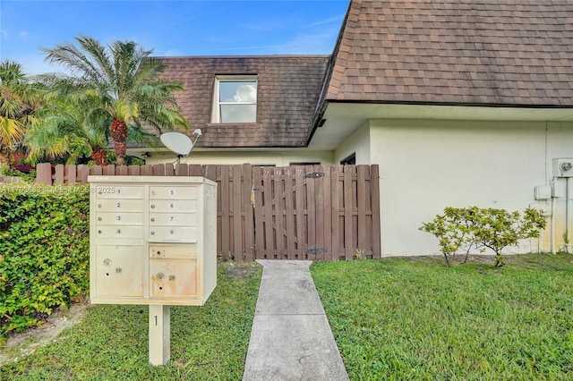 view of home's exterior featuring mail area, roof with shingles, mansard roof, and fence