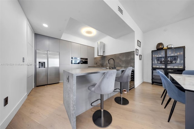 16001 Collins Ave Unit 707, Sunny Isles Beach, FL 33160 - kitchen featuring appliances with stainless steel finishes, a breakfast bar area, gray cabinetry, a peninsula, and decorative backsplash