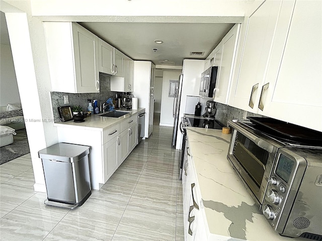 kitchen featuring a sink, decorative backsplash, stainless steel microwave, and light stone countertops