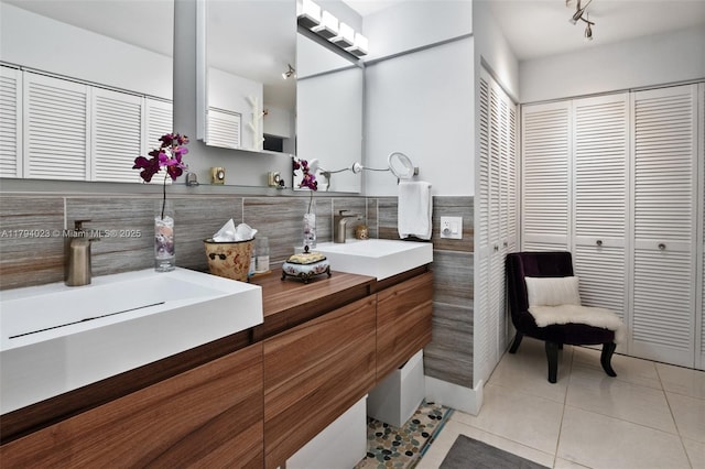 full bathroom featuring a closet, a sink, tile patterned floors, and tile walls