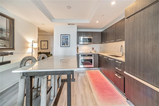 45 SW 9th St Unit 1204, Miami, FL 33130 - kitchen featuring dark brown cabinets, a sink, a raised ceiling, stainless steel appliances, and light wood-type flooring