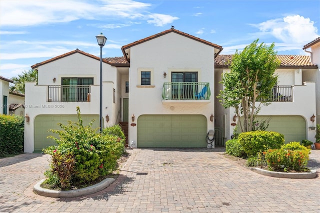 mediterranean / spanish-style home featuring a balcony, decorative driveway, stucco siding, an attached garage, and a tile roof