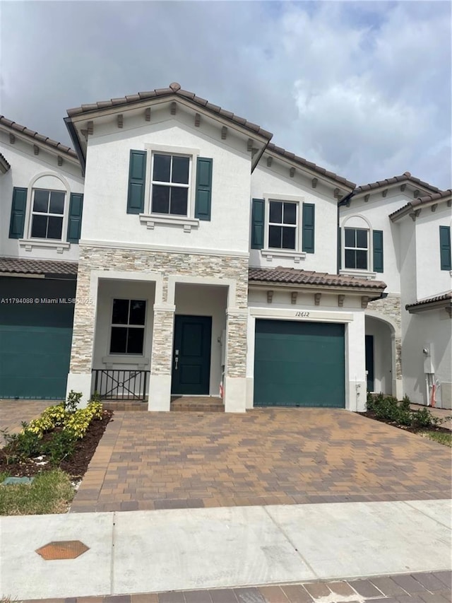 mediterranean / spanish home featuring stucco siding, decorative driveway, a tile roof, and a garage