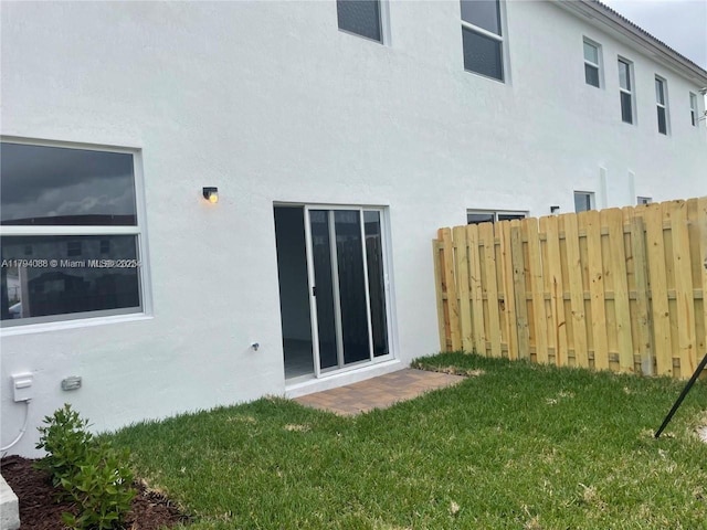 rear view of house with a yard, fence, and stucco siding