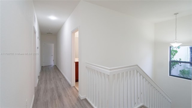 hallway with baseboards, light wood-type flooring, and an upstairs landing
