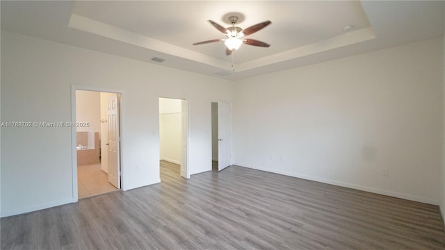 unfurnished bedroom featuring a walk in closet, wood finished floors, a raised ceiling, a closet, and ensuite bathroom