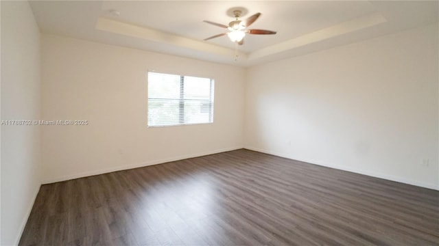 unfurnished room with baseboards, a ceiling fan, a tray ceiling, and dark wood-style floors