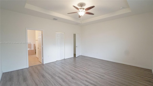 unfurnished bedroom featuring visible vents, wood finished floors, baseboards, a raised ceiling, and connected bathroom