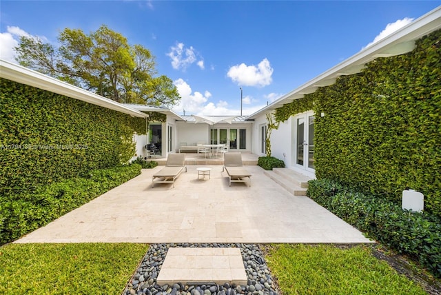 rear view of property featuring french doors, outdoor dining space, a patio area, and stucco siding