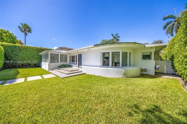 rear view of property featuring a lawn, stucco siding, and a sunroom