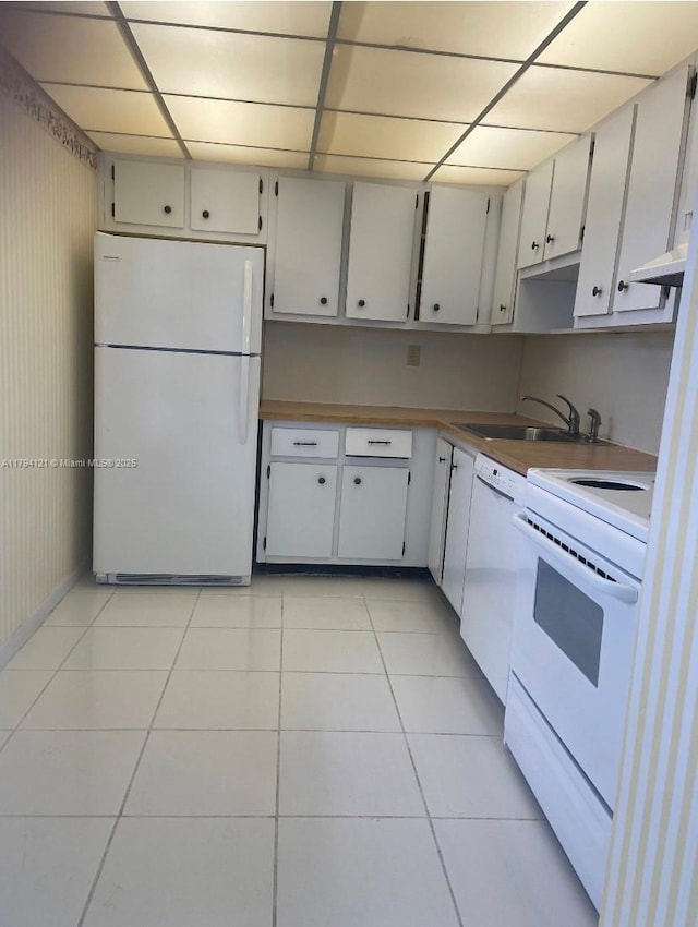 kitchen with a sink, light tile patterned floors, white appliances, and a paneled ceiling