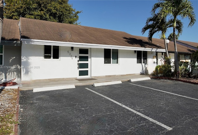 ranch-style house with a shingled roof, uncovered parking, stucco siding, and covered porch