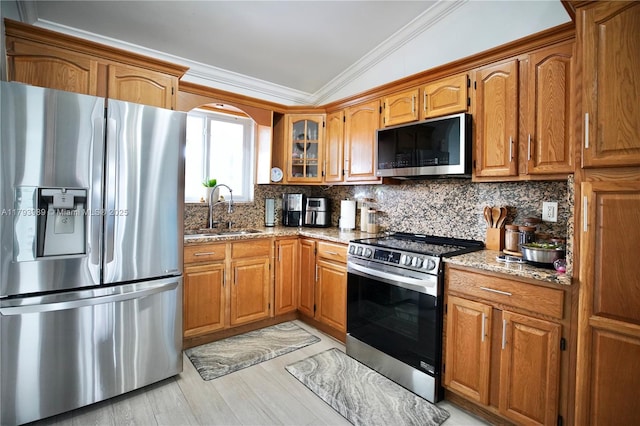 kitchen with crown molding, stainless steel appliances, brown cabinetry, and a sink