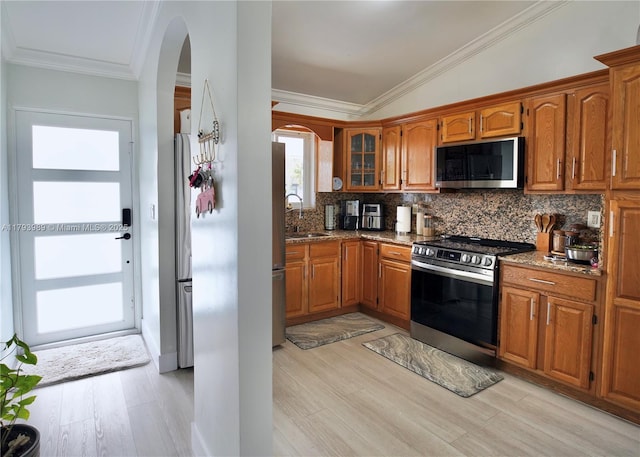 kitchen featuring arched walkways, appliances with stainless steel finishes, brown cabinetry, and light wood-style flooring