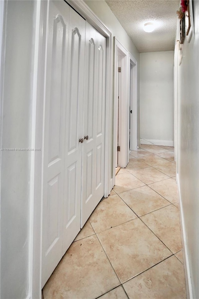 hallway with baseboards, a textured ceiling, and light tile patterned floors