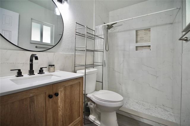 full bath featuring a textured wall, vanity, toilet, a marble finish shower, and wood finished floors