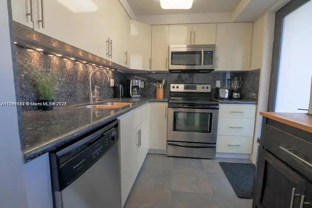 310 Golden Isles Dr Unit 109, Hallandale Beach, FL 33009 - kitchen featuring backsplash, appliances with stainless steel finishes, a sink, light tile patterned floors, and white cabinets