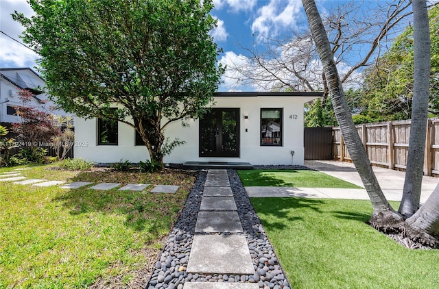 view of front facade featuring fence, a front lawn, and stucco siding