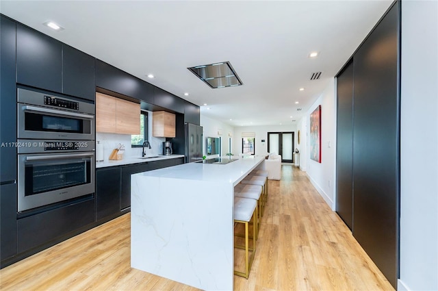 kitchen with modern cabinets, light wood-type flooring, light countertops, dark cabinets, and stainless steel appliances