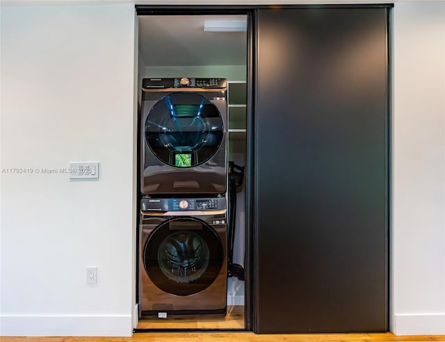 laundry room featuring baseboards, stacked washer / drying machine, wood finished floors, and laundry area