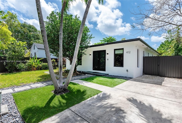 view of front of home with fence, french doors, a front lawn, and stucco siding