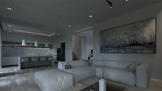 living area with light wood-type flooring, baseboards, and a tray ceiling