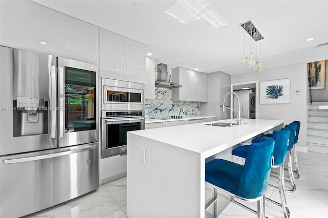 kitchen with appliances with stainless steel finishes, stacked washer and clothes dryer, wall chimney exhaust hood, and marble finish floor