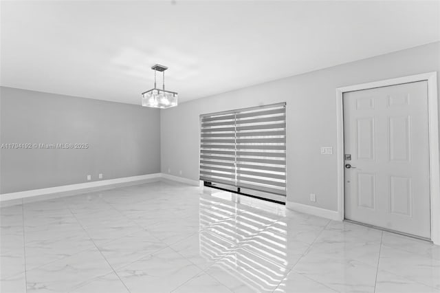 spare room with baseboards, an inviting chandelier, and marble finish floor
