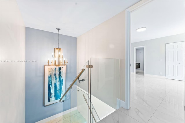 hallway with baseboards, marble finish floor, a notable chandelier, and an upstairs landing
