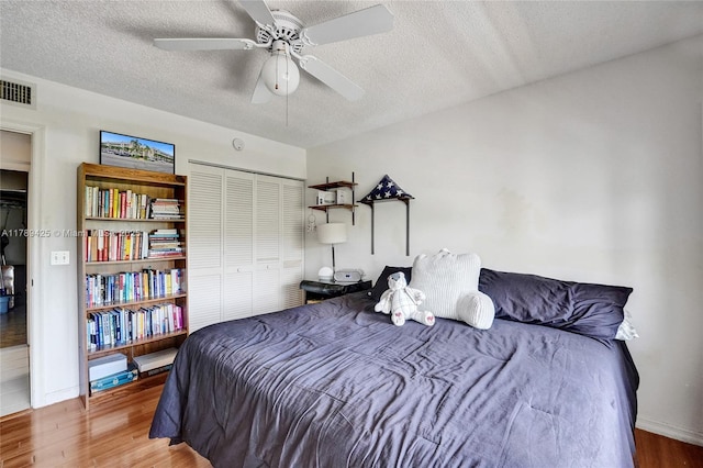 bedroom featuring a textured ceiling, visible vents, wood finished floors, and a closet