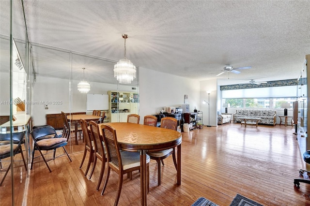 dining space featuring wood-type flooring, ceiling fan with notable chandelier, and a textured ceiling