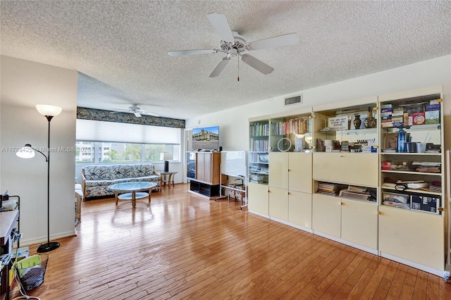 living area featuring visible vents, a ceiling fan, and a textured ceiling