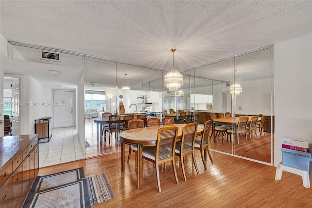 dining area featuring a textured ceiling, light wood finished floors, a chandelier, and visible vents