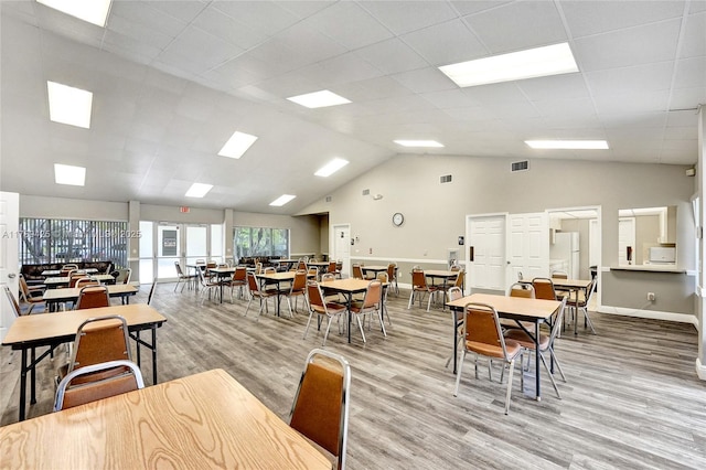 dining room with baseboards, light wood finished floors, visible vents, and high vaulted ceiling