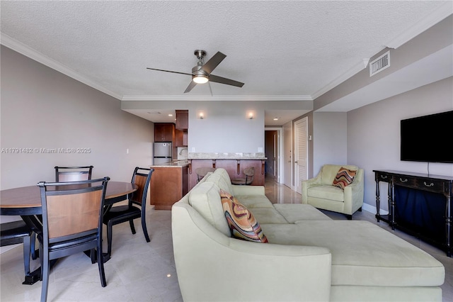 living room with a textured ceiling, a ceiling fan, baseboards, visible vents, and ornamental molding