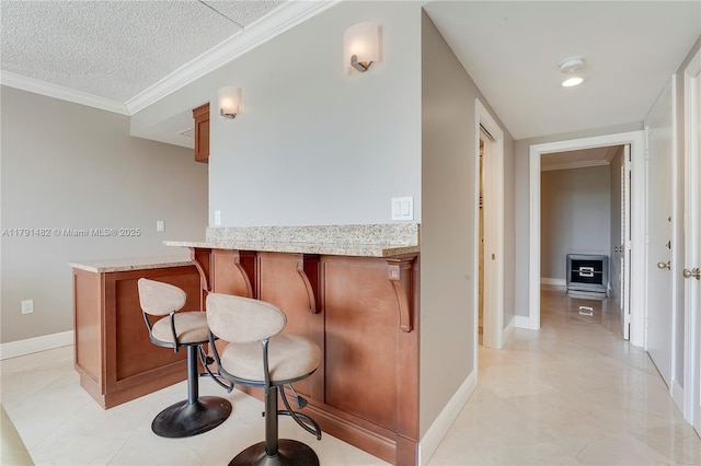 kitchen featuring a kitchen bar, a textured ceiling, brown cabinets, baseboards, and ornamental molding