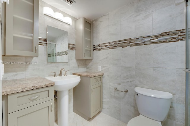 bathroom with visible vents, toilet, tile walls, a sink, and backsplash